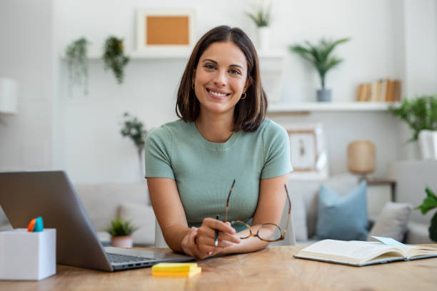 istockphoto-1911998428-612x612 Shot of beautiful business woman working with laptop while looking at camera in living room at home.